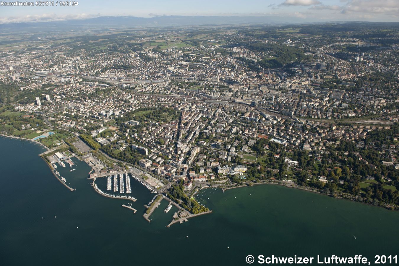 Lausanne, Blickrichtung Nord (Position: 2'537'803.73, 1'152'224.36). - Viertgrösste Stadt der Schweiz nach Basel, Genf und Zürich; Hauptstadt des Kantons Waadt. - Im Bildvordergrund: Freizeithafen und Seepromenade von Ouchy mit dem neugotischen Schloss und diversen markanten Hotelbauten des 19. Jahrhunderts. Rechts am Ufer des Lac Léman: Grünanlagen des Parc Olympique.
